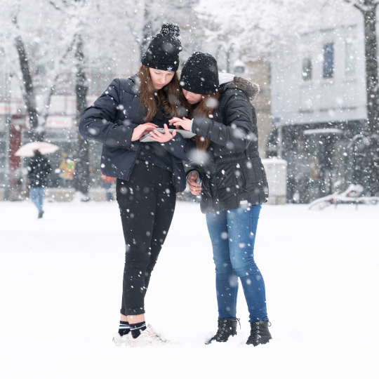 Zwei Jugendliche nutzen digitale Medien im Schnee beim Winterferienprogramm
