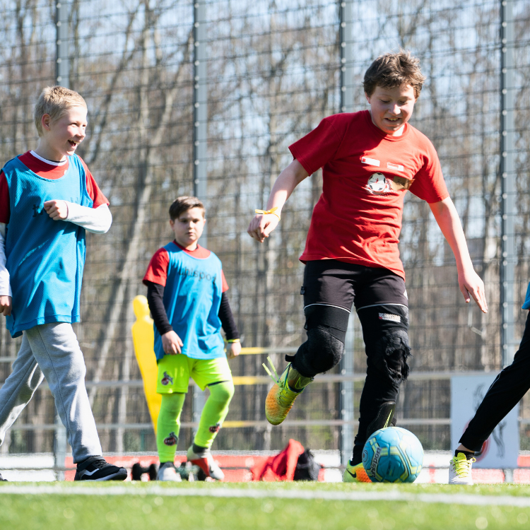 Kinder spielen zusammen Fußball auf einem Sportplatz, betreut von einem pädagogischen Team.