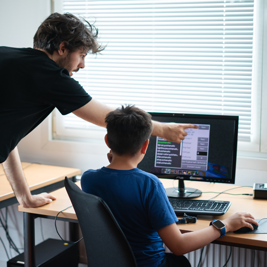 Dozent zeigt Kindern das Programmieren am Computer