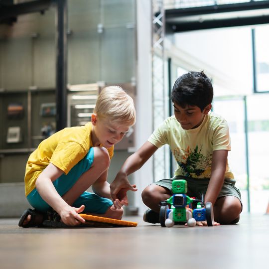 Kinder steuern selbstgebaute Roboter von Robo Wunderkind mit einem Tablet im Robotik-Workshop