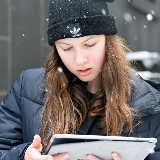 Mädchen beim Winterferienprogramm mit Tablet im Schnee.