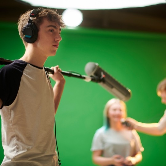 Jugendlicher hält eine Mikrofon-Angel vor einem Greenscreen bei einem Medienprojekttag
